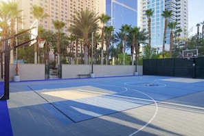 An outdoor basketball court with a blue surface, surrounded by palm trees and tall buildings in the background. - Las Vegas | Pool & Strip Access | Urban Comfort Stay (Las Vegas)