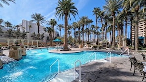A pool area with palm trees, lounge chairs, and a clear blue pool.
