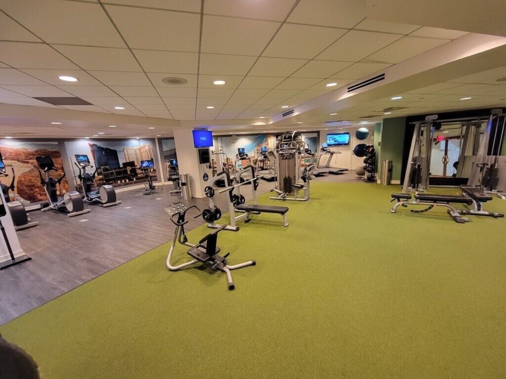 Un gimnasio con varios equipos de ejercicio, incluyendo cintas de correr, bicicletas estáticas y máquinas de pesas.
