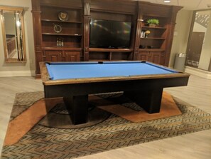 A pool table in a room with wooden cabinets and a television.