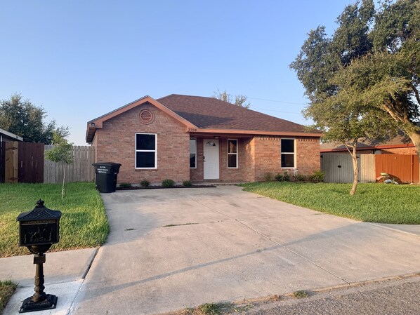 A single-story brick house with a front porch, a garage, and a well-maintained lawn.