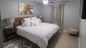 A neatly arranged bedroom with a bed, a ceiling fan, a nightstand, a lamp, a bedside table, a decorative rug, and a wall-mounted TV. - Cozy Home on RGV (Alton)