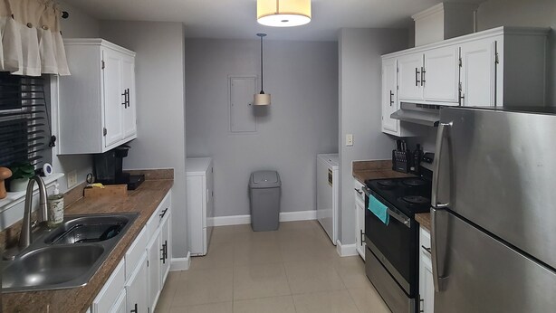 A compact kitchen with white cabinets, a stainless steel refrigerator, a stove, and a sink. - Cozy Home on RGV (Alton)