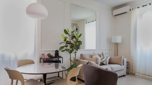 A modern living room with a round glass table, beige chairs, a grey sofa, a potted plant, and a large mirror. - Gemelli Cozy quiet Home- well connected (Roma)