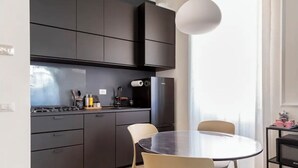 A modern kitchen with dark cabinetry, a round dining table, and a pendant light. - Gemelli Cozy quiet Home- well connected (Roma)