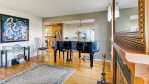 Amplio salón con un piano de cola, un cuadro grande y una zona de comedor con candelabro.