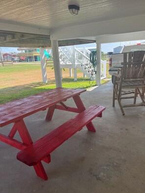 Un espace extérieur abrité comprenant une table de pique-nique rouge, une chaise en bois et une rambarde blanche.