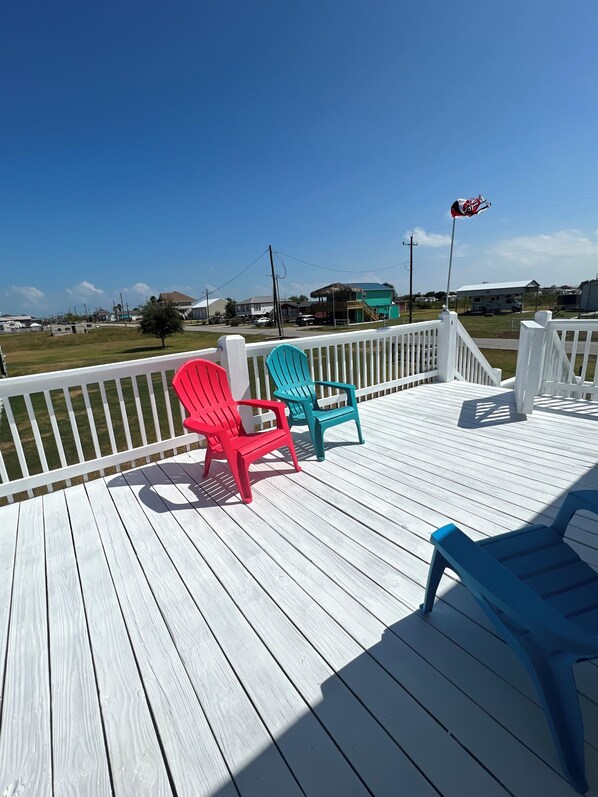 Une terrasse en bois avec trois fauteuils Adirondack de couleur rouge, turquoise et bleue.