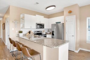 A modern kitchen with white cabinets, a granite countertop, stainless steel appliances, and a bar area with stools.