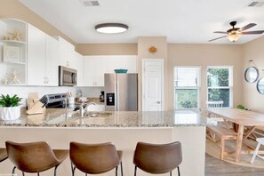 A modern kitchen with white cabinets, a granite countertop, and a dining area with a wooden table and chairs.