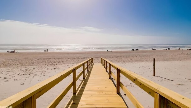 Een houten looppad dat naar een strand leidt, met een heldere lucht en rustige zee.