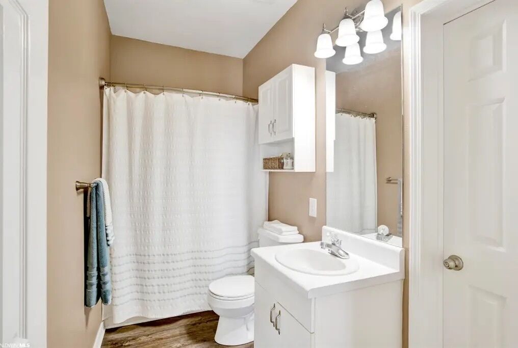 A bathroom with a shower curtain, toilet, sink, and cabinets.