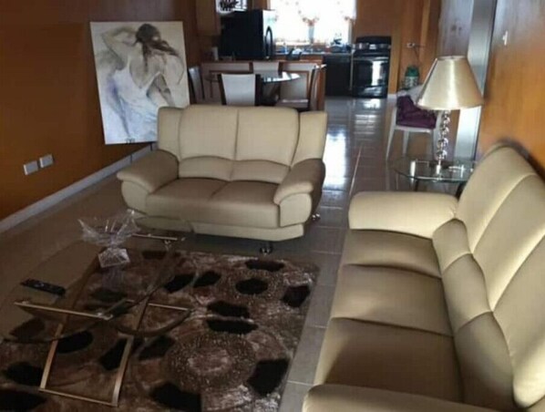 Un salon avec un canapé beige, une table basse surmontée d’un tapis à motifs et un tableau accroché au mur.