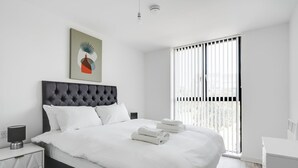A modern hotel room with a large bed, a bedside table, a lamp, and a window with blinds. - GuestReady - Hideaway in Vauxhall (Liverpool)