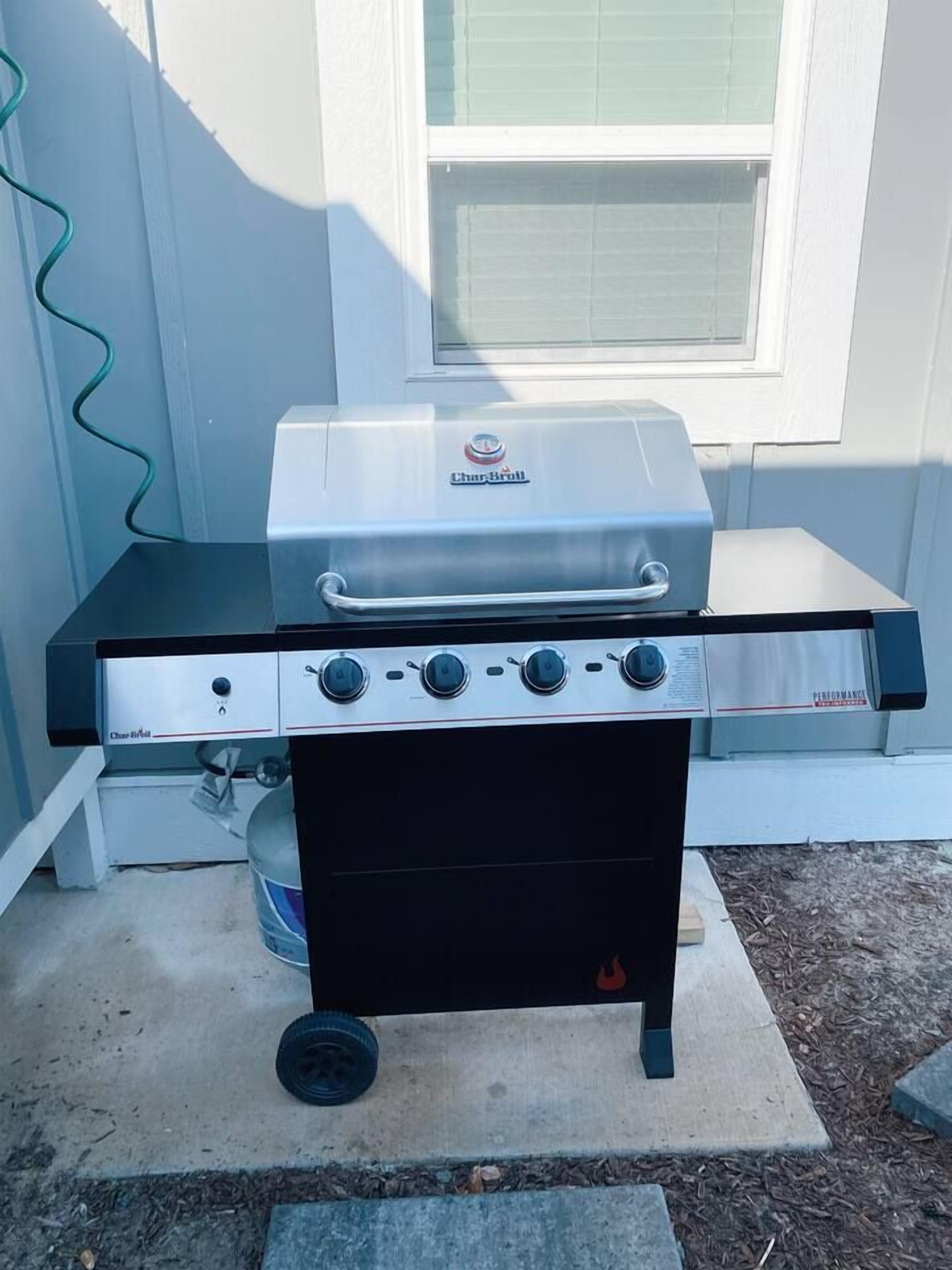 Un barbecue au gaz portatif, doté de quatre brûleurs et d’un brûleur latéral, installé sur une dalle de béton à l’extérieur d’une maison.