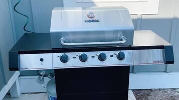 Un barbecue au gaz portatif, doté de quatre brûleurs et d’un brûleur latéral, installé sur une dalle de béton à l’extérieur d’une maison.