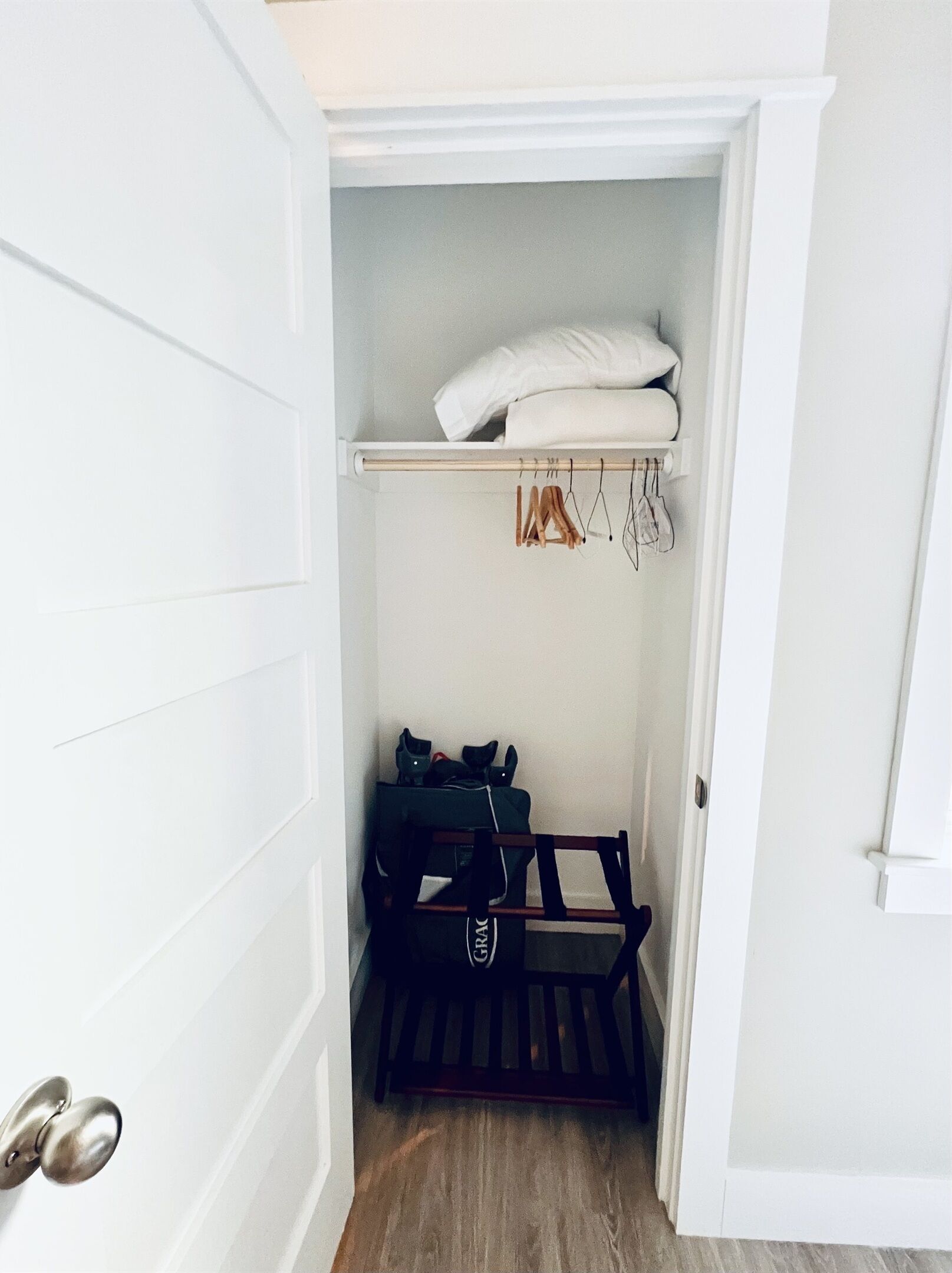 A small walk-in closet with a wooden bench, a hanging rack, and a shelf with folded clothes.