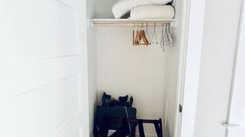 A small walk-in closet with a wooden bench, a hanging rack, and a shelf with folded clothes.