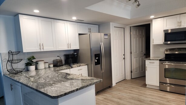 Una cocina moderna con gabinetes blancos, un refrigerador de acero inoxidable, un microondas integrado y una encimera de granito.