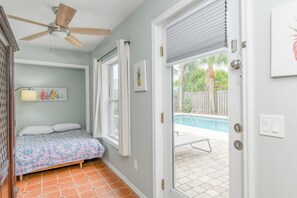Une chambre à coucher avec un lit, un ventilateur de plafond, une fenêtre avec des rideaux et une vue sur une piscine à l’extérieur.