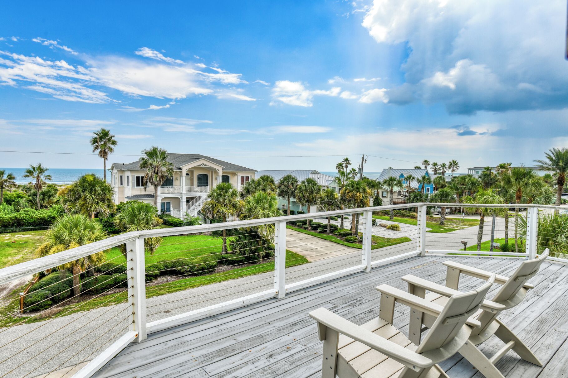 A wooden deck with outdoor seating, overlooking a residential area with houses and a beach.
