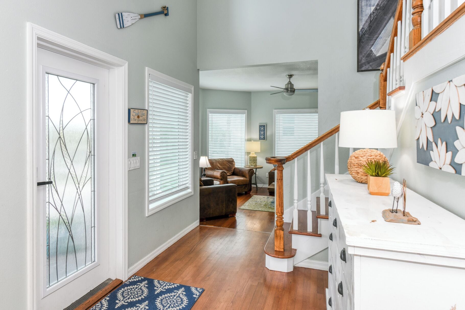 A hallway with a wooden staircase, a white door with a glass panel, and a blue patterned rug.