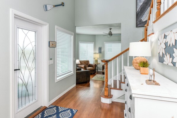 A hallway with a wooden staircase, a white door with a glass panel, and a blue patterned rug.