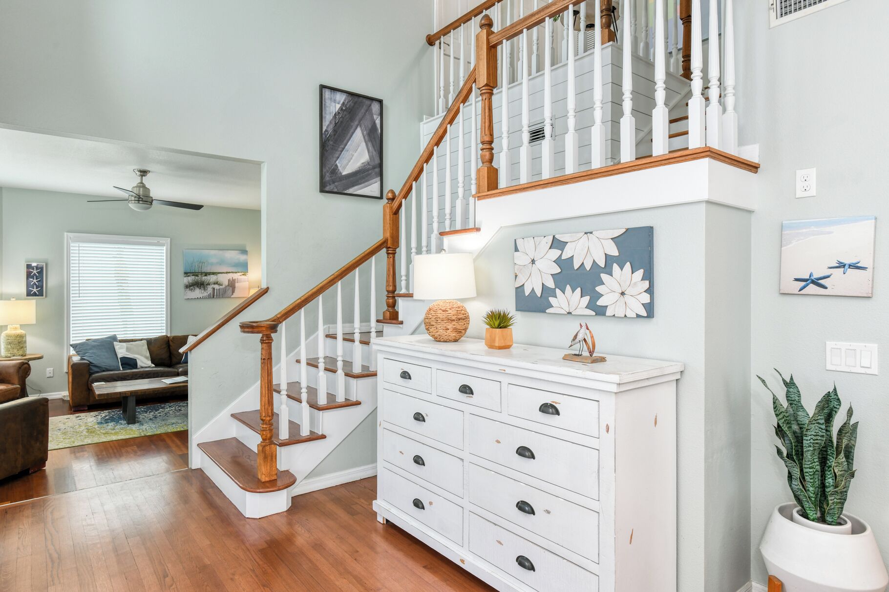A staircase with wooden balusters leading to a landing with a white dresser and a potted plant.