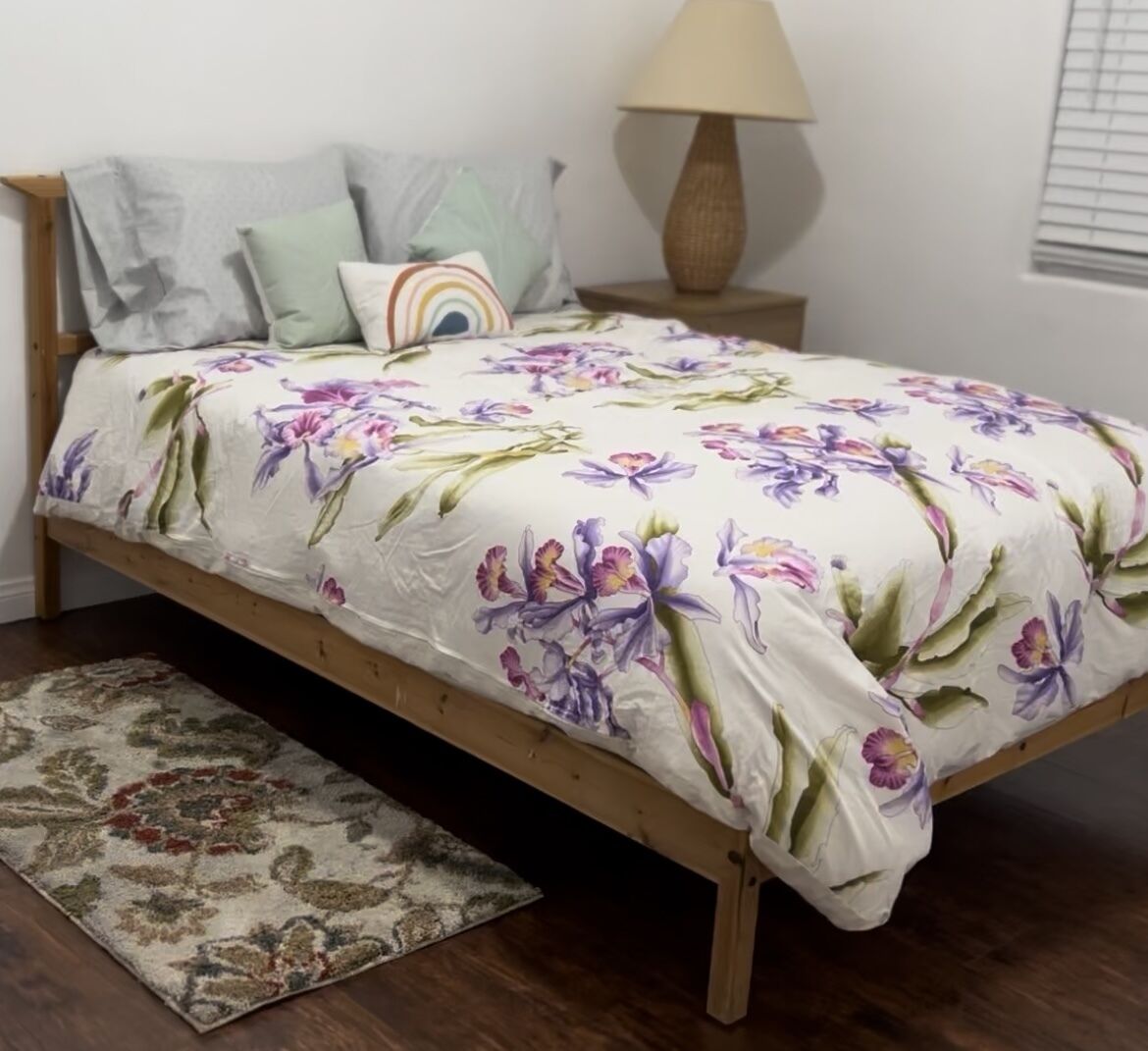 Una cama con colcha estampada, una lámpara de noche y una alfombra con motivos.