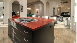 Een moderne keuken met een rood kookeiland, donkere kastjes en een kroonluchter.