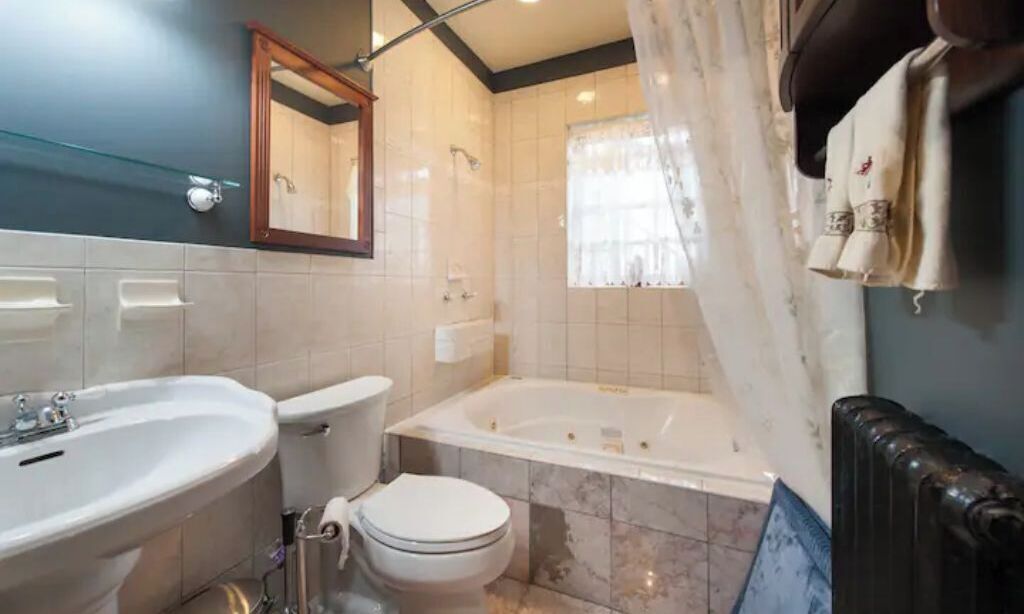 Et badeværelse med vask, toilet, badekar og et spejl.