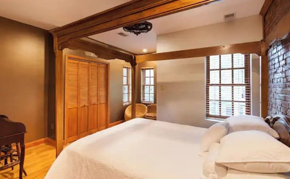 A bedroom with a large bed, wooden ceiling beams, a wardrobe, and a window with blinds.
