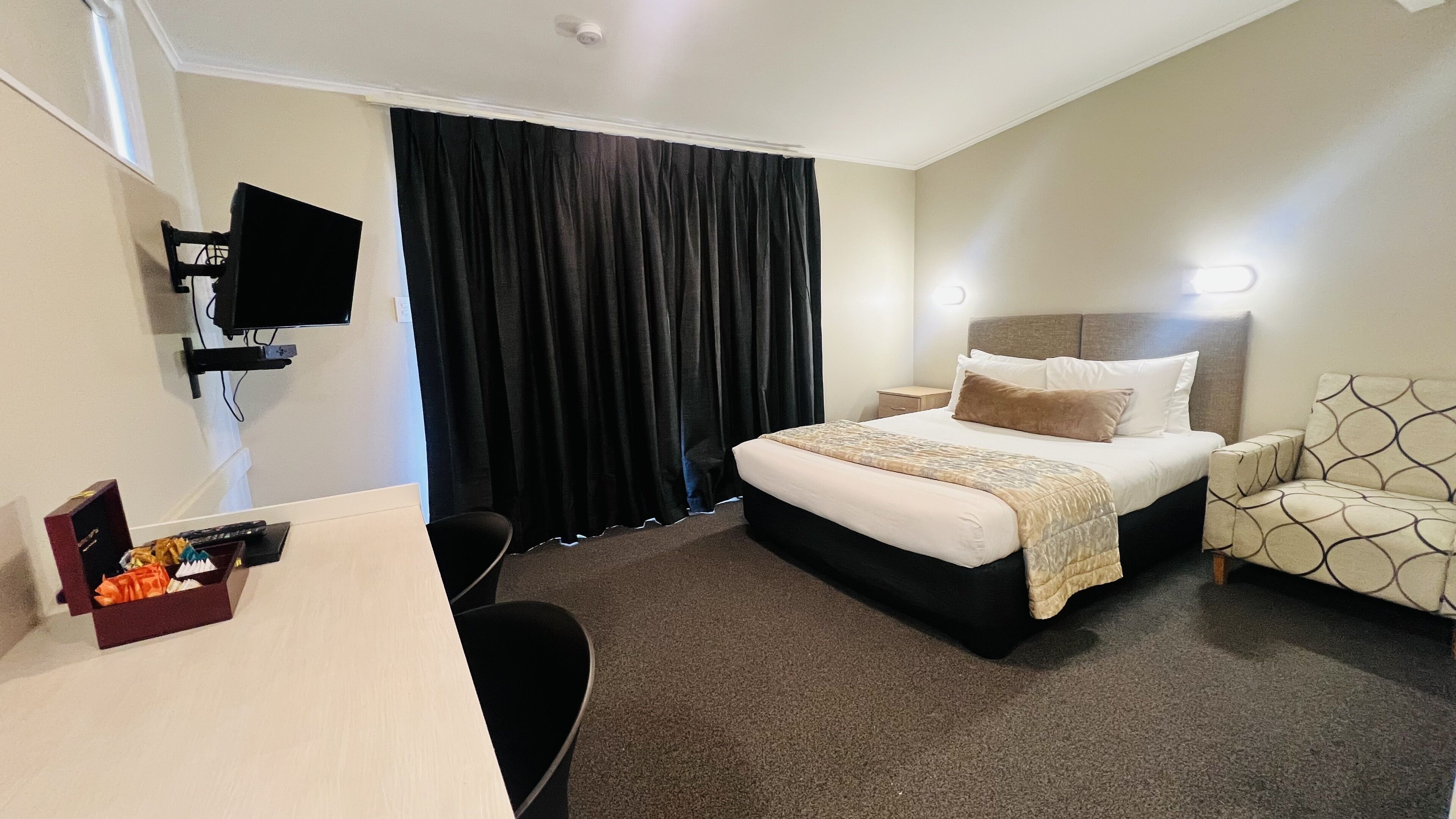 Une chambre d’hôtel avec un lit, une table de chevet, une chaise et un bureau sur lequel se trouvent un ordinateur et quelques objets.