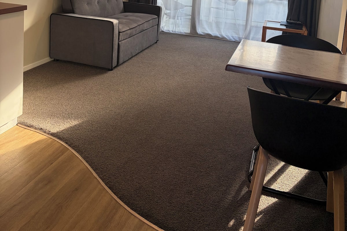 A living room with a grey sofa, a small table, a TV, and a sliding glass door leading to a balcony.