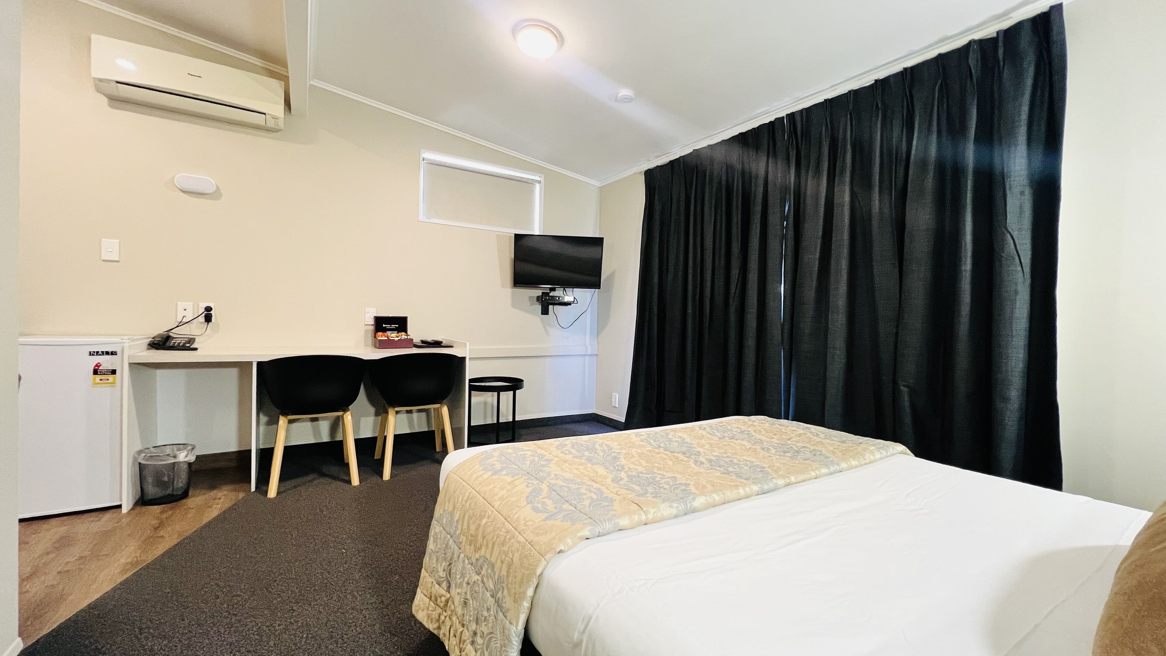 Habitación de hotel con cama, escritorio, dos sillas, televisor y aire acondicionado.