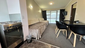 A compact room with a kitchenette, a sofa bed, a dining table with chairs, and a TV. - Marineland Motel (Napier)