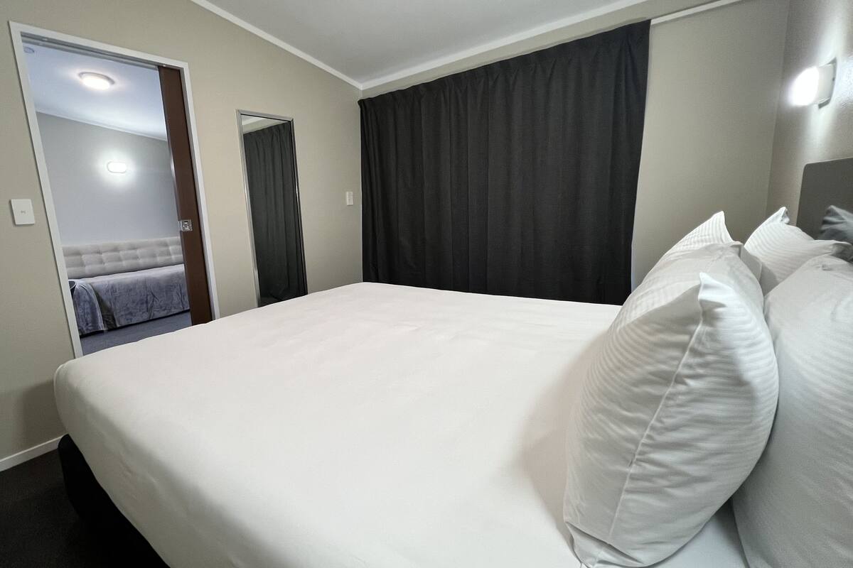 A hotel room with a large bed, a mirror, a door leading to another room, and a light fixture on the ceiling.