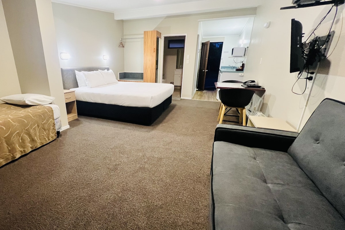 A hotel room with a single bed, a sofa, a desk, and a small kitchenette.