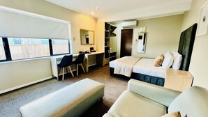 A hotel room with a bed, a desk, a chair, a closet, and a window. - Marineland Motel (Napier)