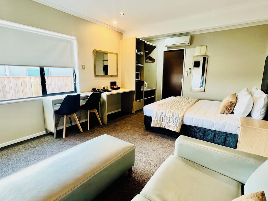 Une chambre d’hôtel avec un lit, un bureau, une chaise, une armoire et une fenêtre.