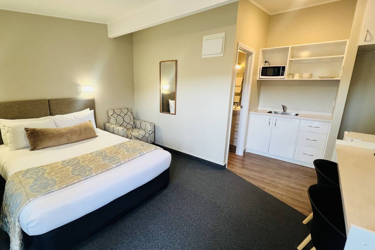 A hotel room with a large bed, a desk, a chair, a microwave, and a small kitchenette.