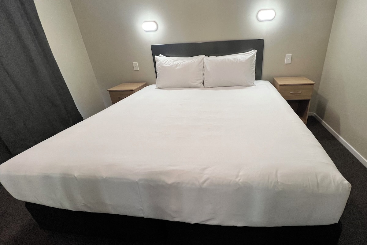 A hotel room with a large bed, two bedside tables, and a headboard with integrated lighting.