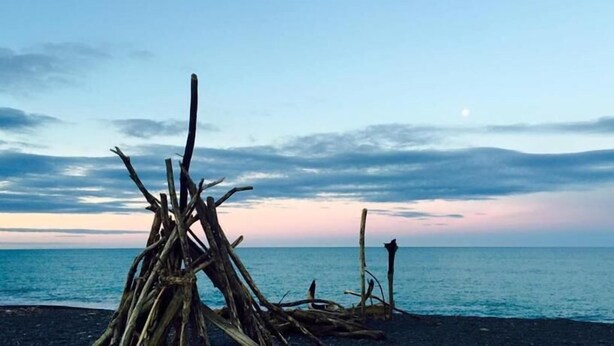 A beach scene with driftwood structures and a calm sea under a partly cloudy sky. - Marineland Motel (Napier)
