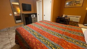 Een slaapkamer met een bed, een bureau, een stoel, een televisie, een spiegel en een verwarming.