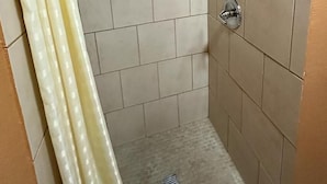 Een badkamer met beige tegels, een douchegordijn en een afvoer.