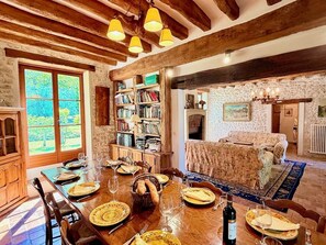 Un coin repas avec une table en bois dressée pour le repas, une bibliothèque et un salon confortable avec un canapé.