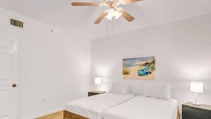 A bedroom with two beds, a ceiling fan, a painting of a beach scene, and bedside lamps. - Luxury beachfront condo with magnificent views (North Redington Beach)
