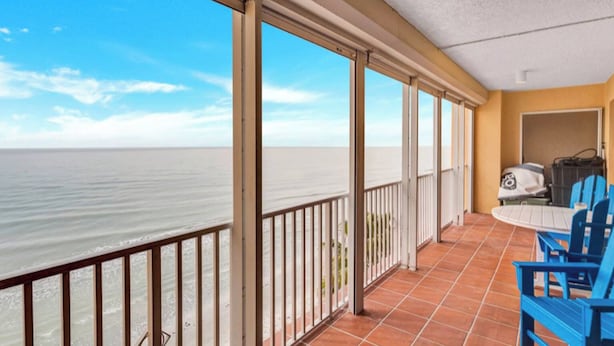 A balcony with a view of the ocean, a table with chairs, and a door leading to an interior room. - Luxury beachfront condo with magnificent views (North Redington Beach)