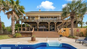 A two-story house with a pool, palm trees, and a wooden deck.