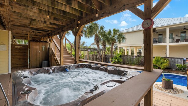 A wooden deck with a hot tub, a pool, and a covered area with a clock.